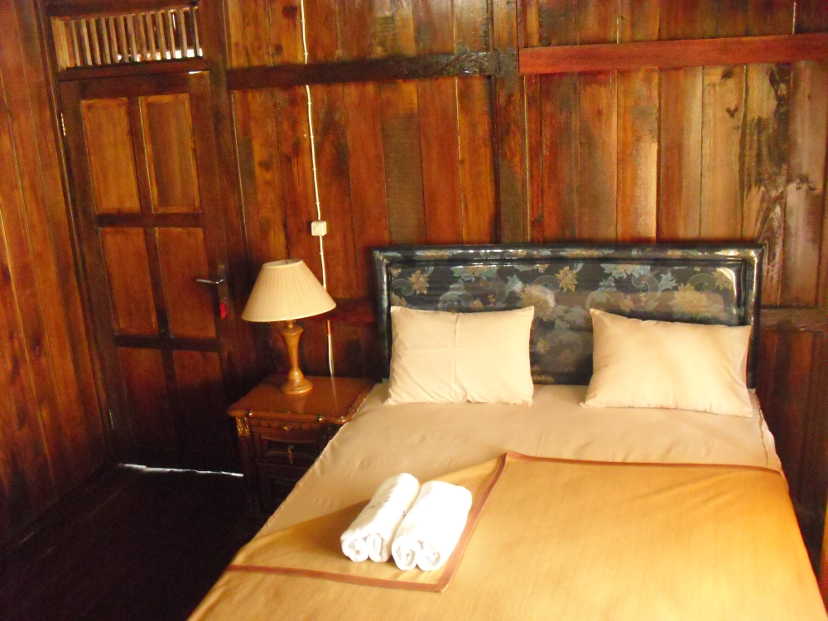 Queen-size bed with batik head board and brown bed cover in a wooden guest house